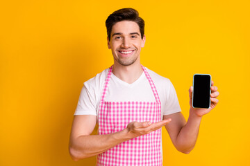 Photo portrait of guy demonstrating with hand showing phone with blank space isolated on vivid yellow colored background