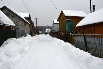 A cloudy winter day. Snowfall. A street in a dacha village. Snow-covered cleared road and...