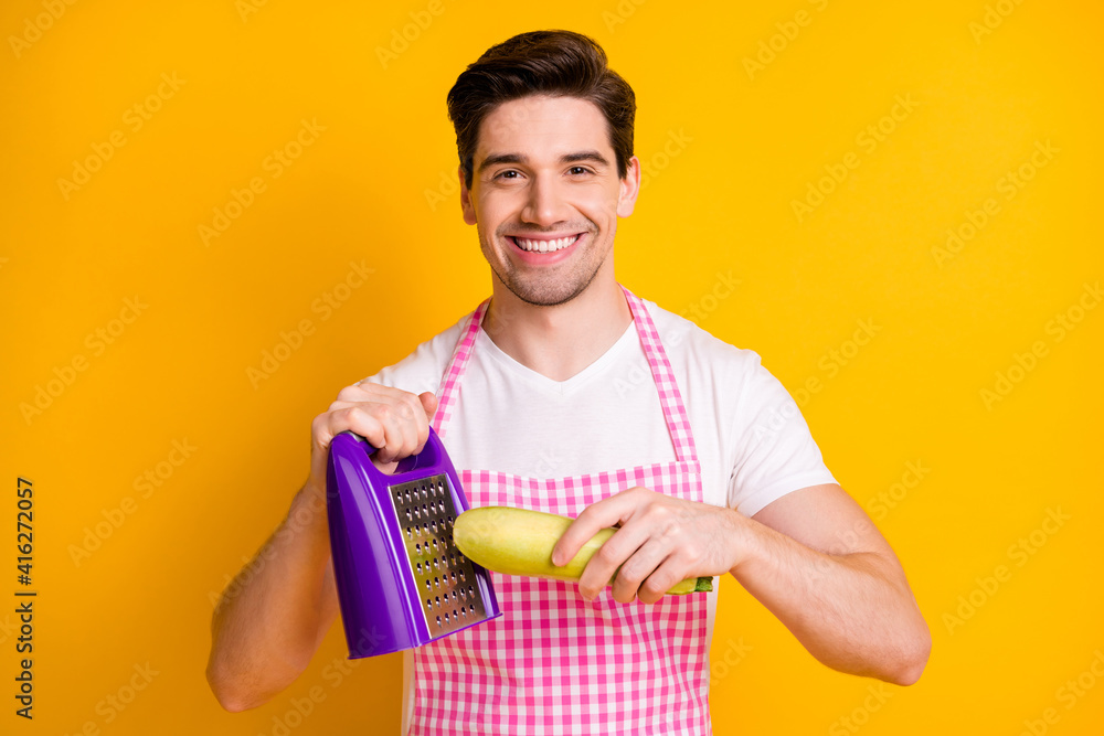 Wall mural Photo portrait of smiling man grating squash isolated on vivid yellow colored background