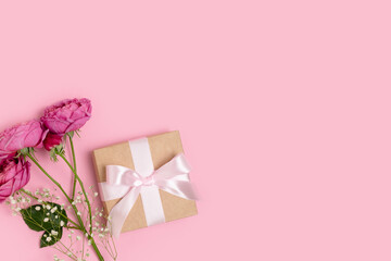 Present with a tied ribbon and bouquet of flowers on a pink pastel background. Gift for 8 March or Mothers Day with copyspace.