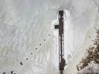 Fishing pier in the middle of the frozen river. Aerial drone view. Foggy winter morning.