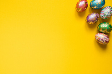 Painted Easter eggs with golden foil on the yellow background. Copy space.