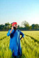 Naklejka na ściany i meble Young indian farmer talking on smartphone at wheat field