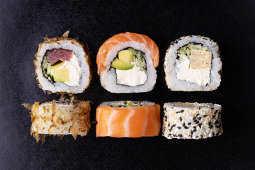 Sushi rolls set with avocado, cheese, salmon and tuna on black background. Top view.