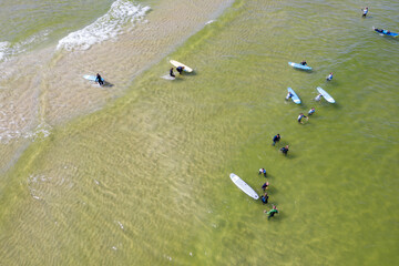 Aerial drone view of people surfing in the sea. Summer sport learning how to surf. Surfboarding in...