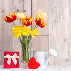 Tulip flowers for Mother's Day greeting in glass vase over wooden table and wall.