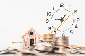 double exposure of analog alarm clock and miniature house with blurred stack of coins, business and finance background