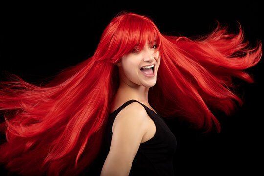 Laughing red-haired girl with fluttering hair. Beautiful young woman with healthy long hair in close up portrait isolated on black