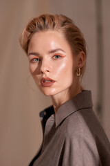Elegant woman with fashionable make-up wearing grey linen blazer posing aginst beige textile...