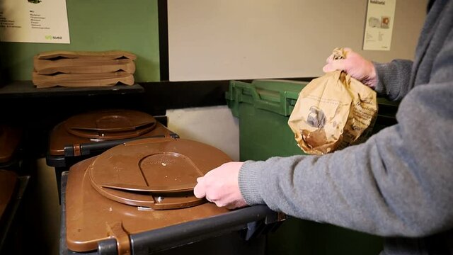 A brown bag of organic waste is disposed of.