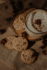 Beautiful creamy coffee in a cup with cookies and brownies carefully placed on the wooden surface with a brown background covered with beams of sunlight