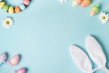 Easter frame with bunny ears, eggs, white flowers on pastel blue background. Top view. Happy Easter holiday. Greeting card.