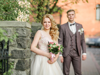 happy bride with wedding bouquet standing on city street