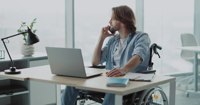 Young handsome office employer boss in wheelchair talking business partner conversation dialing smartphone in corporate office.
