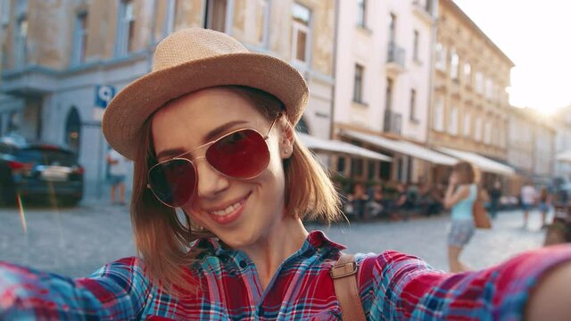 Close up portrait of young beautiful girl tourist in sunglasses and hat standing on background of architectural memo holding camera and smiling.