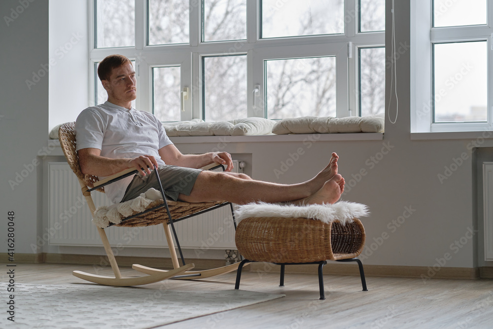 Wall mural Young man relaxing on cozy rocking-chair in light room. Joy of life. Total relaxation.