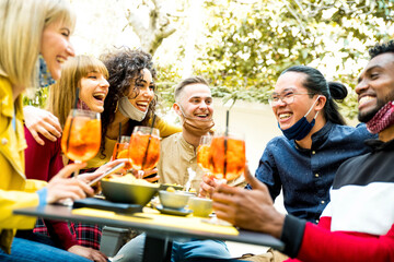 Multiracial friends wearing face masks drinking cocktails at bar restaurant - New normal friendship concept with young people enjoying meal in backyard party - Focus on guy in the middle