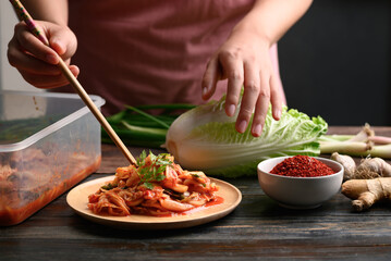 Kimchi cabbage on wooden plate decoration with coriander leaf by woman hand, Homemade Korean food