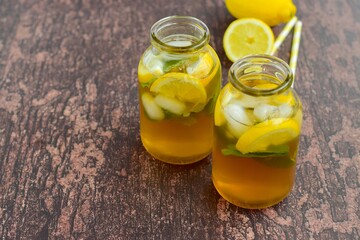 Iced tea with lemon slices and mint leaves on rustic background