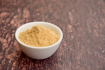 Bowl of maca powder on wooden background