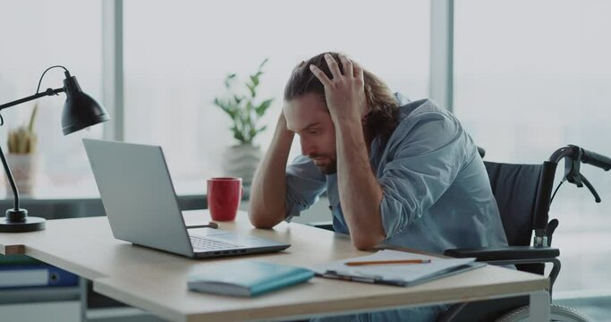 Young depressed office worker sitting by desk worry about work. Disabled invalid young man frutrating having problems at work.