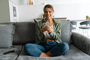 Happy nice woman using mobile phone while sitting on sofa