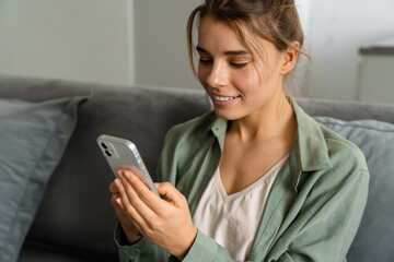 Happy nice woman using mobile phone while sitting on sofa