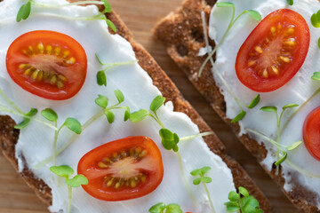 Rye crisp bread with creamy vegetarian cheese tofu, cherry tomato and rucola micro greens on wooden desk. Healthy food, gluten free, diet concept. 