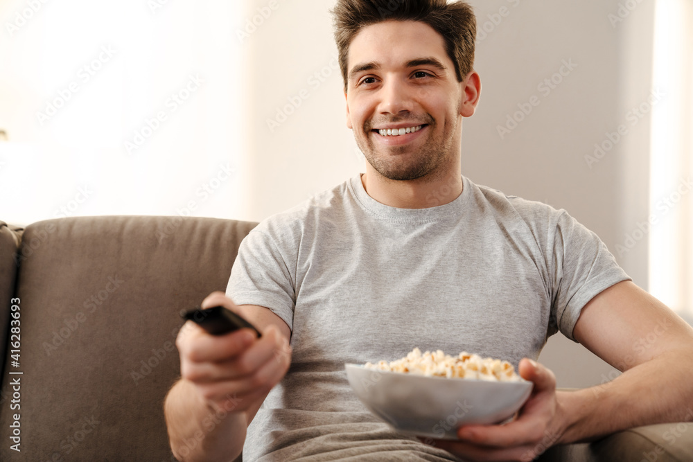 Wall mural Happy man watching tv and eating popcorn