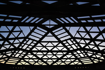 Silhouette of roofing construction.Wooden roof frame with sun shining trough slats and rafters, against the blue sky. Building under development.