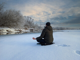 Fototapeta na wymiar A young man meditates in the snow near a mountain river. Outdoor wellness concept.