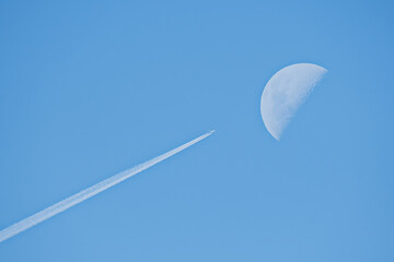 Fototapeta na wymiar Airplane with condensation trails flying next to the moon on the blue sky