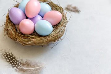 Happy Easter concept. Preparation for holiday. Colorful decorated easter eggs in nest with feather on concrete stone grey background. Simple minimalism flat lay top view copy space.