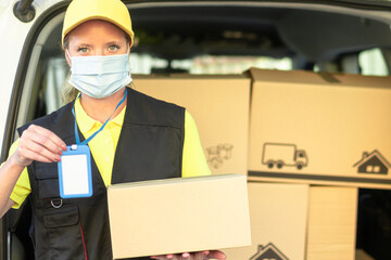 Portrait of woman courier with delivering package, with protective mask for coronavirus. Copy space on blue identification card and package. Medical, delivery transport and express delivery.