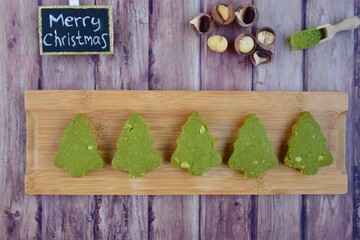 Green tea Matcha Christmas tree cookies with Macadamia on wood background. Merry Christmas letter...