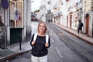Fototapeta premium Traveling by Portugal. Happy young woman with rucksack walking by streets in Lisbon.