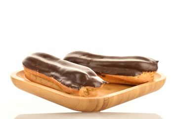Two sweet chocolate eclairs on a bamboo tray, close-up, isolated on white.