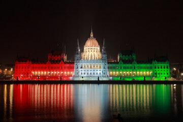 The hungarian Parliament by night lit in national colors red, white and green on the Danube bank;...
