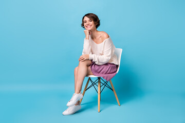Full length photo portrait of dreamy girl holding head sitting in chair isolated on pastel blue...