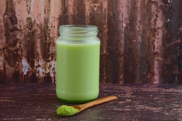 Cold refreshing iced matcha latte drink in glass jar. Wooden background. Clean eating, healthy, vegetarian, vegan, alkaline diet, dairy free food concept
