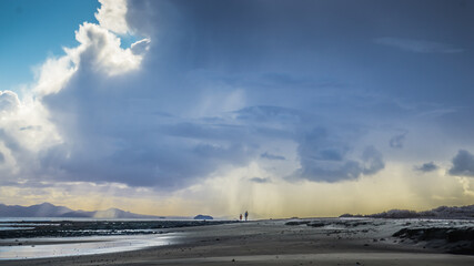 Padre e hijo pasean por una larga playa con gran cantidad de nubes sobre ellos mientras llueve