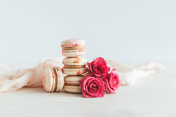 Tasty french macaroons with pink roses on a white wooden background.