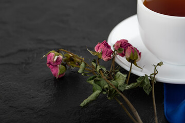 Dried roses with a cup of hot tea on a black background