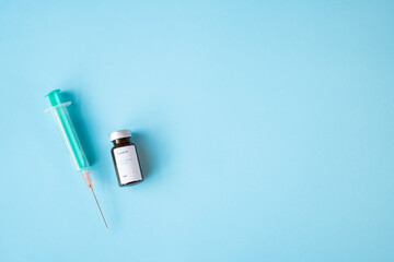 A vial of coronavirus vaccine, a syringe with a needle, with a blue background. Copyspace