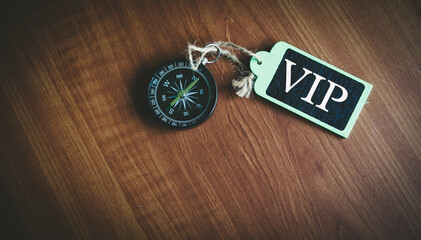 VIP text written on wooden tag with magnetic compass on old wooden background. A business concept.