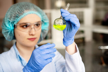 The student prepares a solution for a lesson in chemistry or biotechnology. The girl holding fluorescent yellow solution