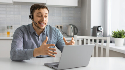 Fototapeta premium Young man in front of laptop with headset during an online video call.