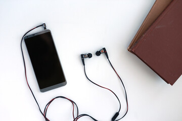 Smartphone, books and earphones with black and red cable on white table