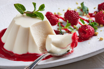 Spoon with a piece of panna cotta with syrup, raspberries and mint in oval plate, food stylind,...
