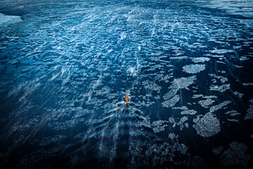 Tugboat driving through frozen sea surrounded by dark waters with ice blocks floating in sea. 